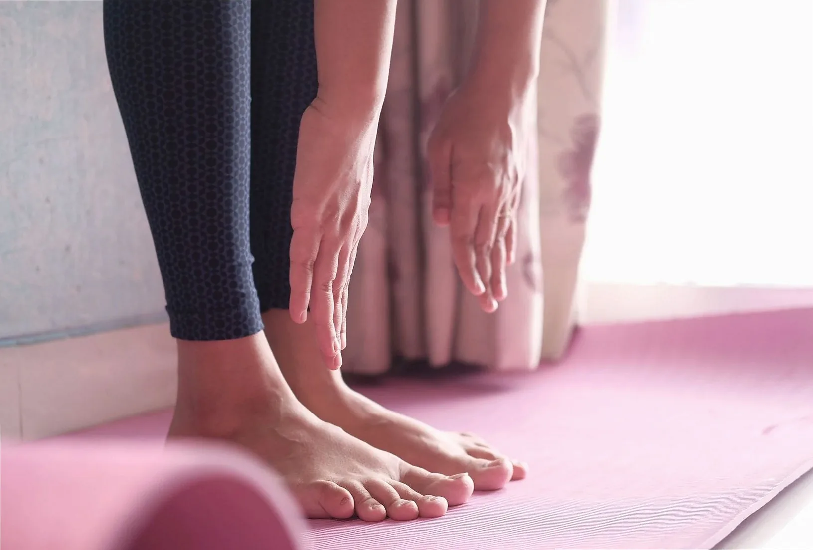 Close-up of a person doing a yoga pose on a pink mat indoors, showing feet and hands.
