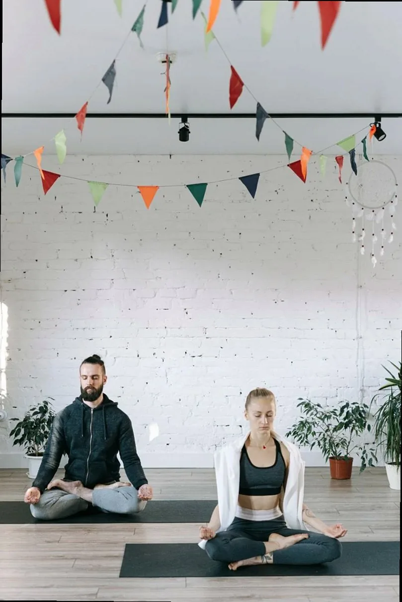 A man and woman practicing meditation in a serene yoga studio adorned with colorful flags.